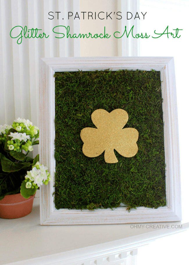 cut out of gold glitter shamrock on imitation moss in a white frame