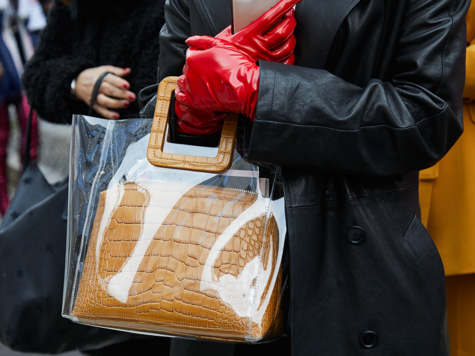 Frau auf der Straße, die eine durchsichtige Plastiktasche und rote Handschuhe trägt