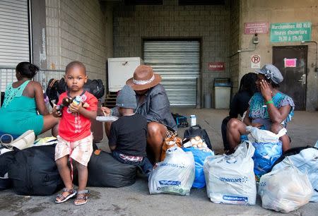 A group of Haitian asylum seekers sit with shopping bags outside the Olympic Stadium, which is being used for temporary housing for asylum seekers, in Montreal, Quebec, Canada August 2, 2017. Picture taken August 2, 2017. REUTERS/Christinne Muschi