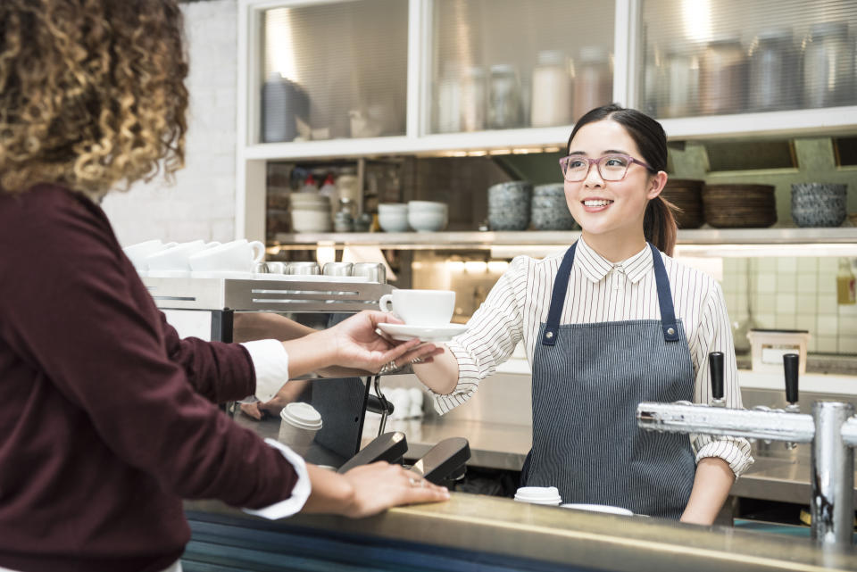 Woman handing coffee cup to customer in cafe.