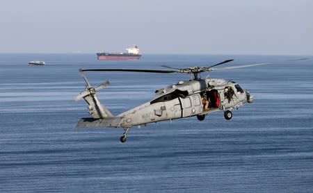 FILE PHOTO: An MH-60S helicopter hovers with an oil tanker in the background as the USS John C. Stennis makes its way to the Gulf through the Strait of Hormuz