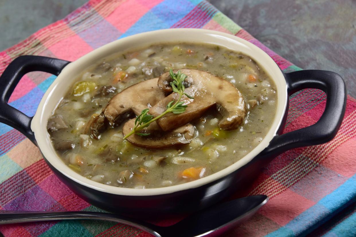 Homemade mushroom and barley soup with wild mushrooms, carrots, and pearl barley, garnished with a sprig of fresh thyme.