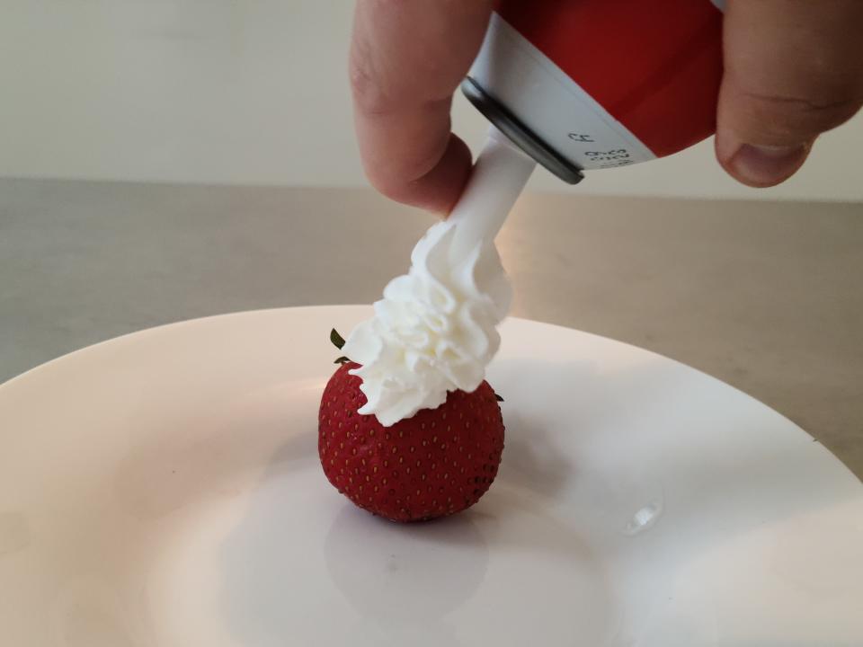 hand spraying can of farmland whipped cream onto a strawberry