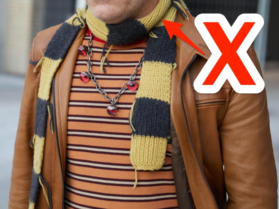 red x and arrow pointing at a man's black and yellow thin scarf wrapped around his neck