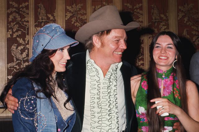 <p>Michael Ochs Archives/Getty</p> Country singers and sisters Loretta Lynn (on left) and Crystal Gayle flank Loretta's husband Mooney Lynn at a soiree in circa 1976.