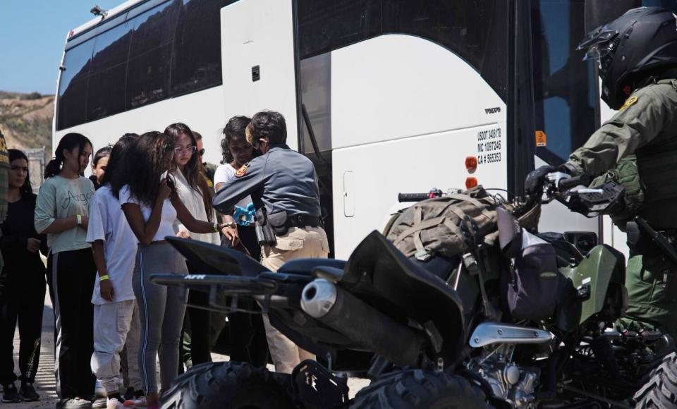 Two women near a bus are handcuffed