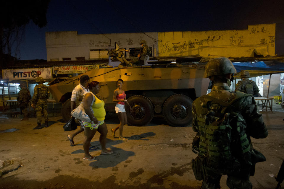 Residents walk past an armored vehicle during an operation to occupy the Mare slum complex in Rio de Janeiro, Brazil, Saturday, April 5, 2014. More than 2,000 Brazilian Army soldiers moved into the Mare slum complex early Saturday in a bid to improve security and drive out the heavily armed drug gangs that have ruled the sprawling slum for decades. (AP Photo/Silvia Izquierdo)