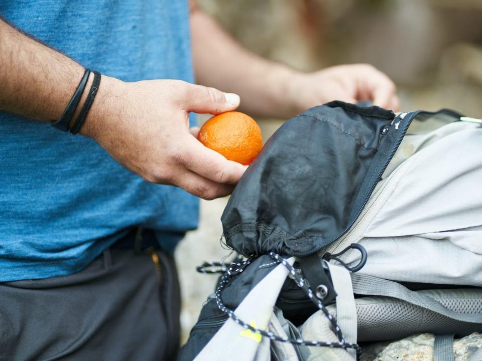 A person packs an orange into their backpack.