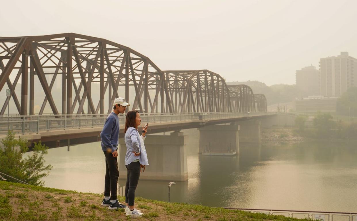Two people stand as the South Saskatchewan River is enveloped by forest fire smoke in Saskatoon, Sask., on Sunday, Sept. 3, 2023. (Heywood Yu/The Canadian Press - image credit)