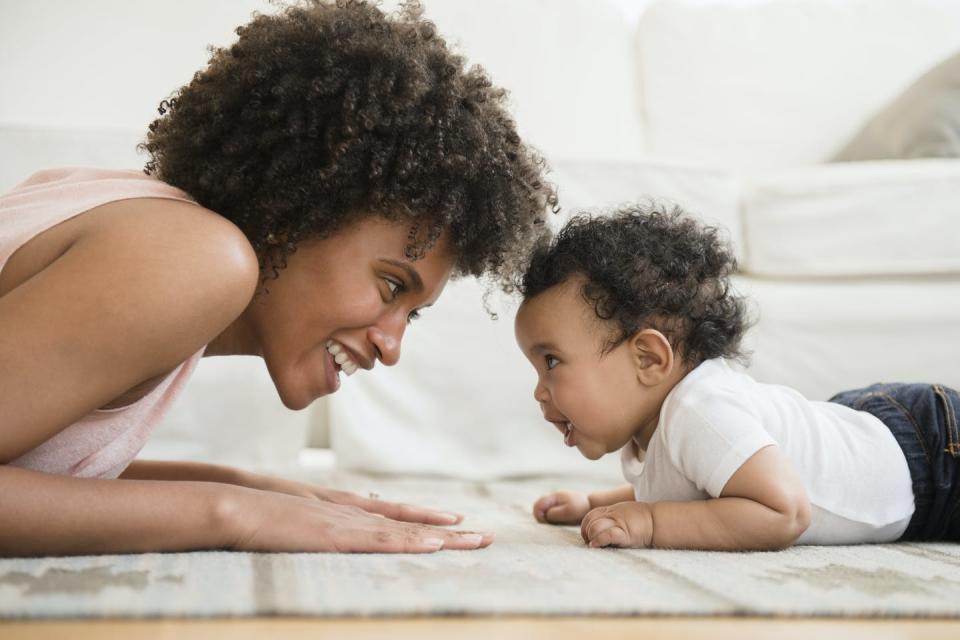 Mother playing face to face with baby son on floor.