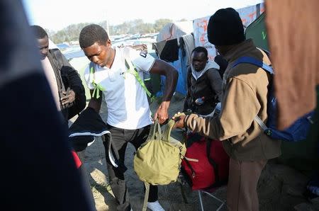 A migrant carries his belongings as he walks past tents and makeshift shelters on the second day of their evacuation and transfer to reception centers in France, during the dismantlement of the camp called the "Jungle" in Calais, France, October 25, 2016. REUTERS/Neil Hall