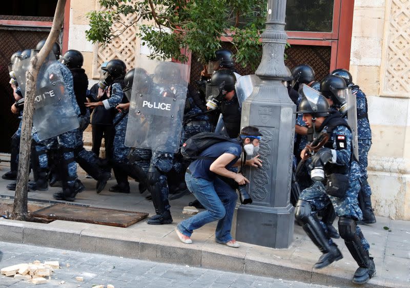 A photographer takes cover as policemen withdraw while demonstrators throw stones during a protest in Beirut