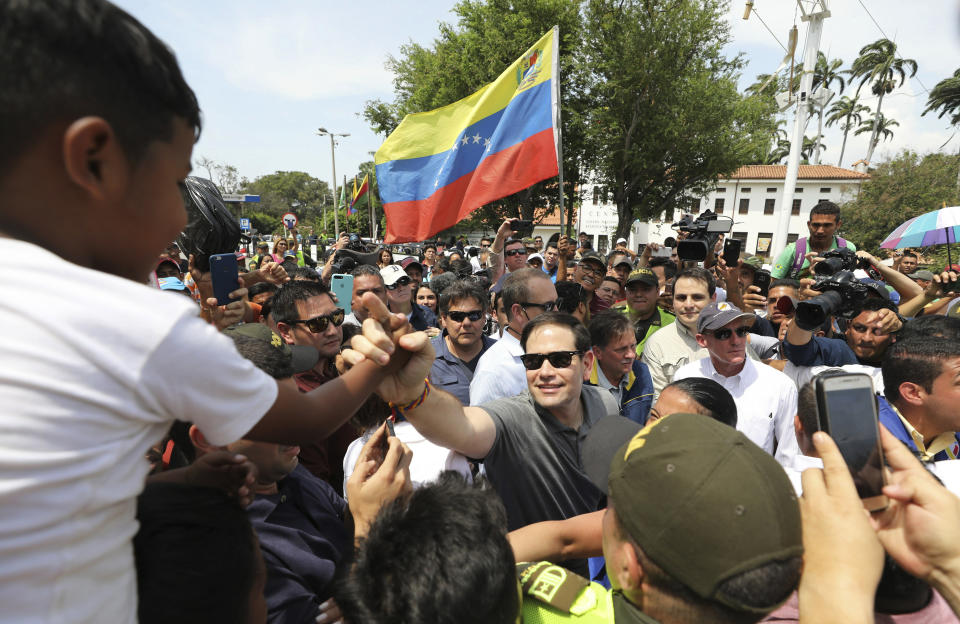 U.S. Senator Marco Rubio, R-Fla., greets Venezuelan migrants near the Simon Bolivar International Bridge, which connects Colombia with Venezuela, where one holds up Venezuelan flag in La Parada, near Cucuta, Colombia, Sunday, Feb. 17, 2019. As part of U.S. humanitarian aid to Venezuela, Rubio is visiting the area where the medical supplies, medicine and food aid is stored before it it expected to be taken across the border on Feb. 23. (AP Photo/Fernando Vergara)