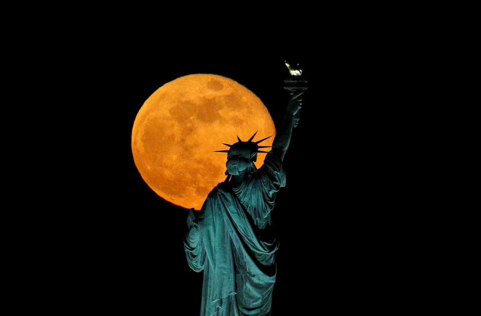 The full moon, also known as the Supermoon or Flower Moon, rises above the Statue of Liberty, as seen from Jersey City, New Jersey, U.S., May 7, 2020. REUTERS/Brendan McDermid     TPX IMAGES OF THE DAY