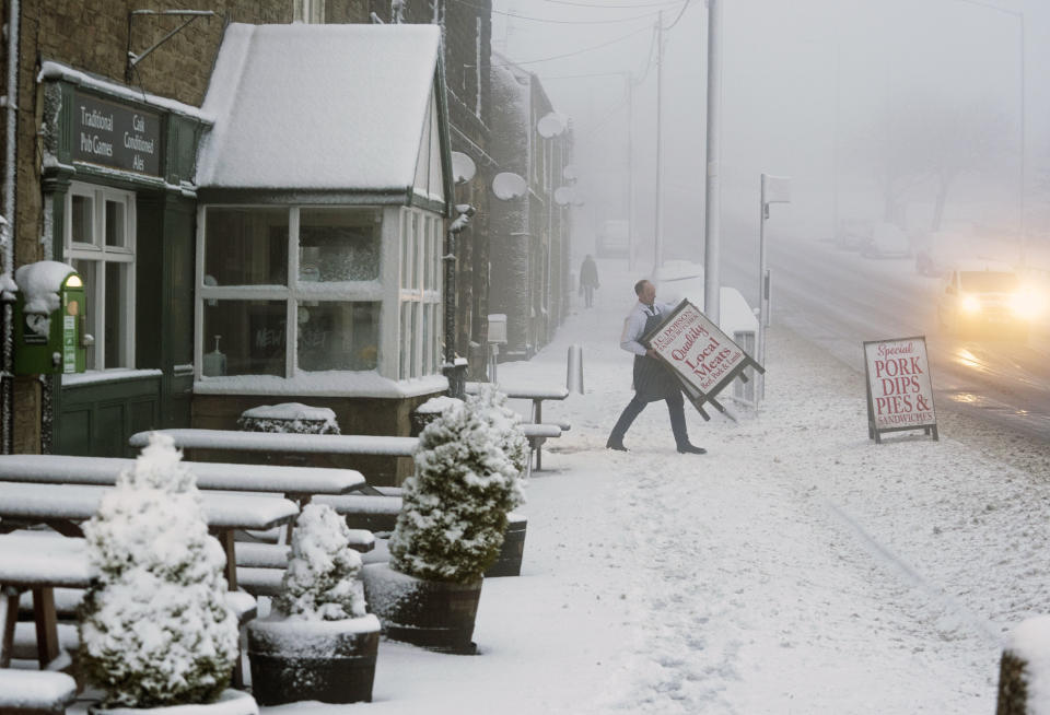 A local butcher carries his shop sign across a snowy pavement in Tow Law, County Durham, Britain, as Storm Eunice makes landfall Friday, Feb. 18, 2022. Millions of Britons are being urged to cancel travel plans and stay indoors Friday amid fears of high winds and flying debris as the second major storm this week prompted a rare “red” weather warning across southern England. (Owen Humphreys/PA via AP)