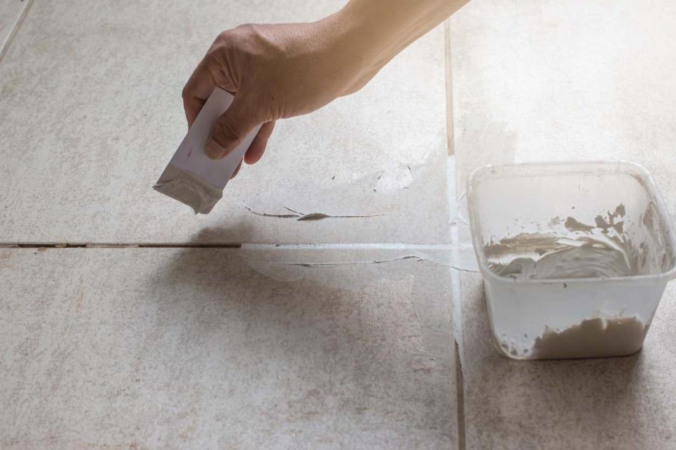 A close up of a hand using a white tool to regrout tiles.