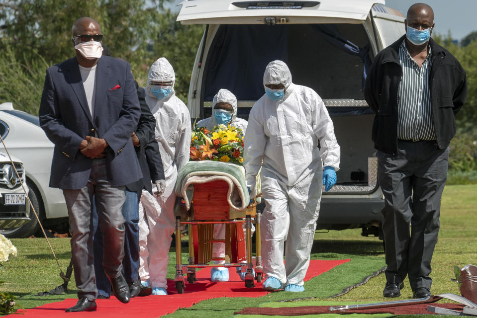 FILE - In this April 16, 2020, file photo, pallbearers wearing personal protective equipment suits lift the casket containing the remains of Benedict Somi Vilakasi for his burial ceremony at the Nasrec Memorial Park outside Johannesburg, South Africa. Africa’s confirmed coronavirus cases have surpassed 1 million, but global health experts tell The Associated Press the true toll is several times higher. (AP Photo/Jerome Delay, File)