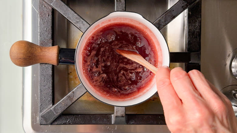 Raspberry sauce boiling in saucepan with wooden spoon stirring