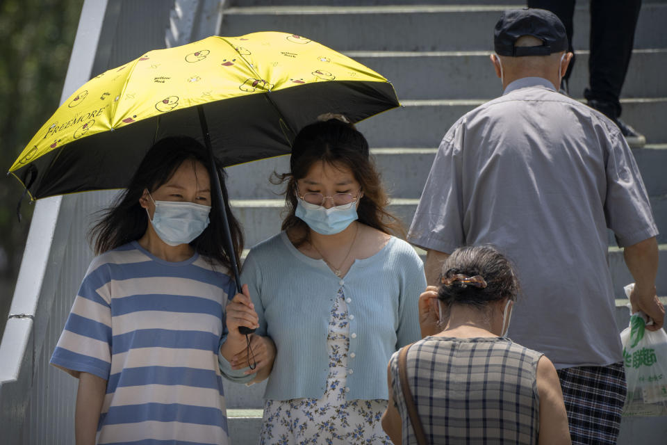 Women wearing face masks carry an umbrella as they walk across a pedestrian overpass in Beijing, Thursday, June 30, 2022. (AP Photo/Mark Schiefelbein)