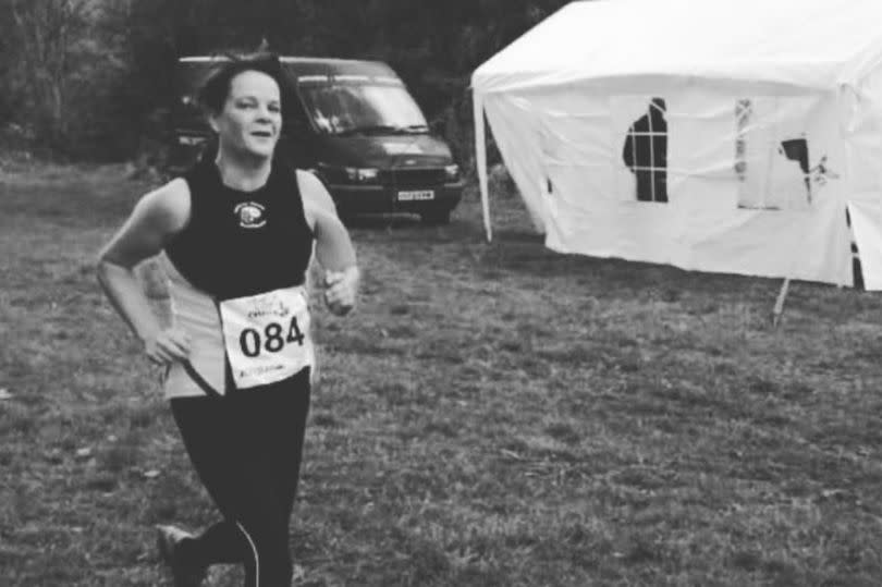 A black and white photo of Janet running in a vest top with the running number 84 on the front, in a field next to a marquee tent