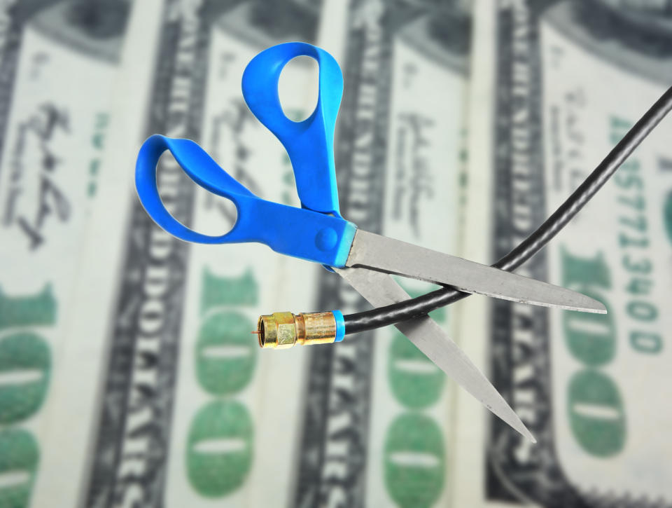 Scissors cut a cable cord in front of cash.