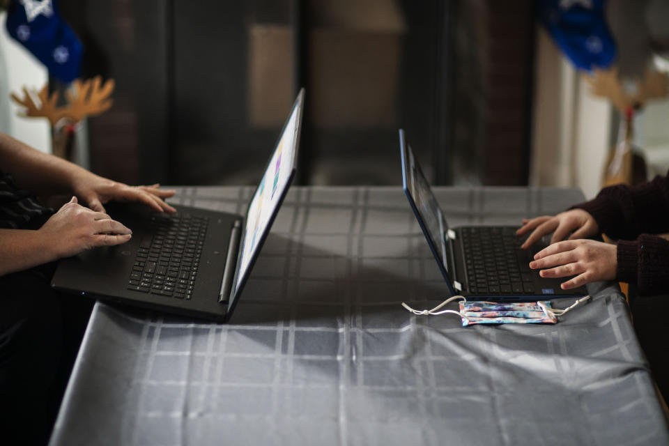 Eileen Carroll, left, works on her laptop as her daughter, Lily, 11, attends school remotely from their home in Warwick, R.I, Wednesday, Dec. 16, 2020. When Carroll's other daughter tested positive for the coronavirus, state health officials told her to notify anyone her daughter might have been around. Contact tracers, she was told, were simply too overwhelmed to do it. It's the same story across the U.S., as a catastrophic surge in infections has made it difficult or impossible to keep up with the calls considered critical to controlling outbreaks. (AP Photo/David Goldman)