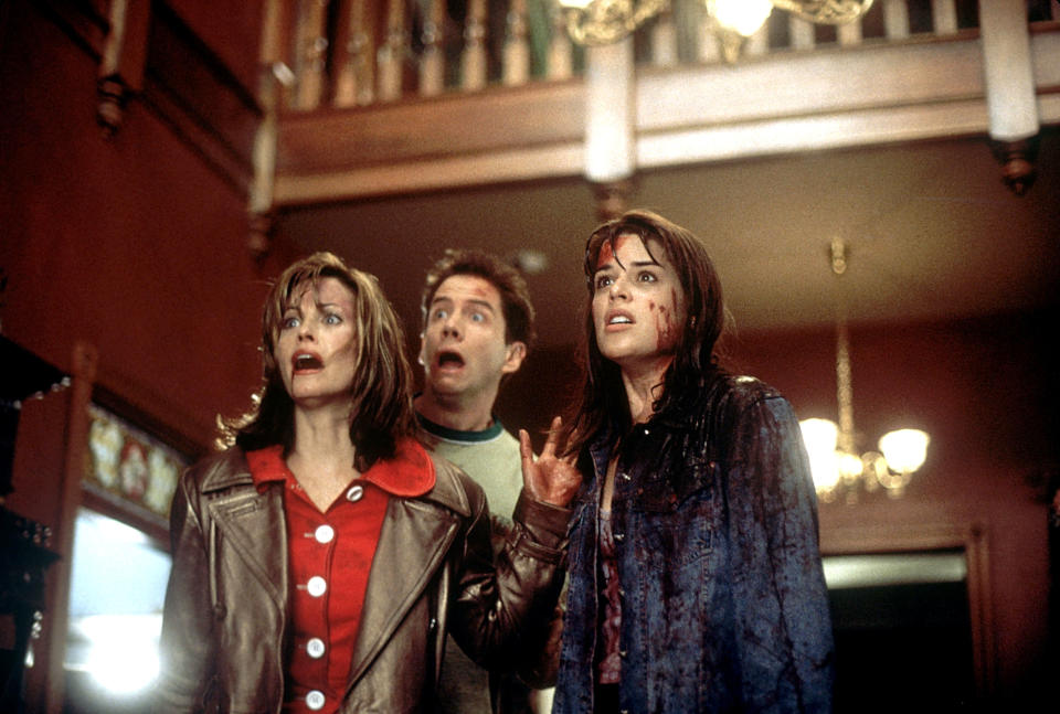 Courtney Cox, David Arquette, and Neve Campbell in a suspenseful scene from "Scream," with all three looking shocked and fearful