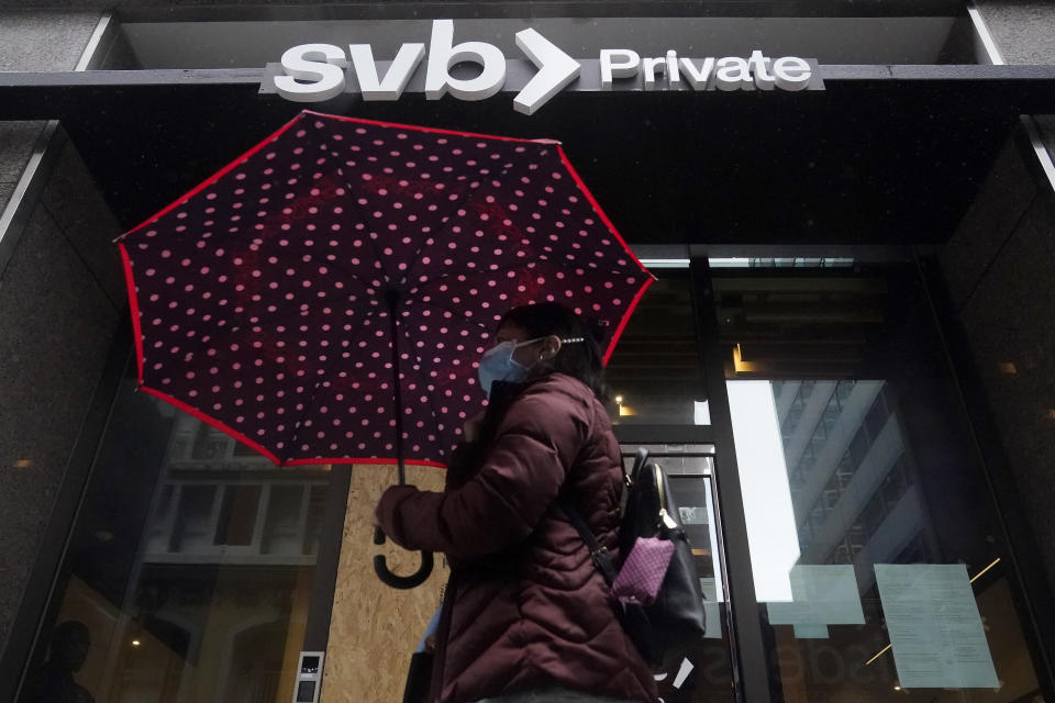 A pedestrian carries an umbrella while walking past a Silicon Valley Bank Private branch in San Francisco, Tuesday, March 14, 2023. After a frenetic weekend of round-the-clock briefings, U.S. policymakers took the audacious step guaranteeing all the deposits of the failed Silicon Valley Banks, even those exceeding the FDIC's $250,000 limit. (AP Photo/Jeff Chiu)