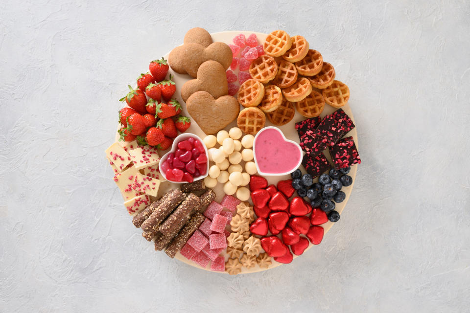 Charcuterie Valentines Day board with chocolate, red hearts, different sweets, strawberries, blueberries and candies on light gray background. View from above