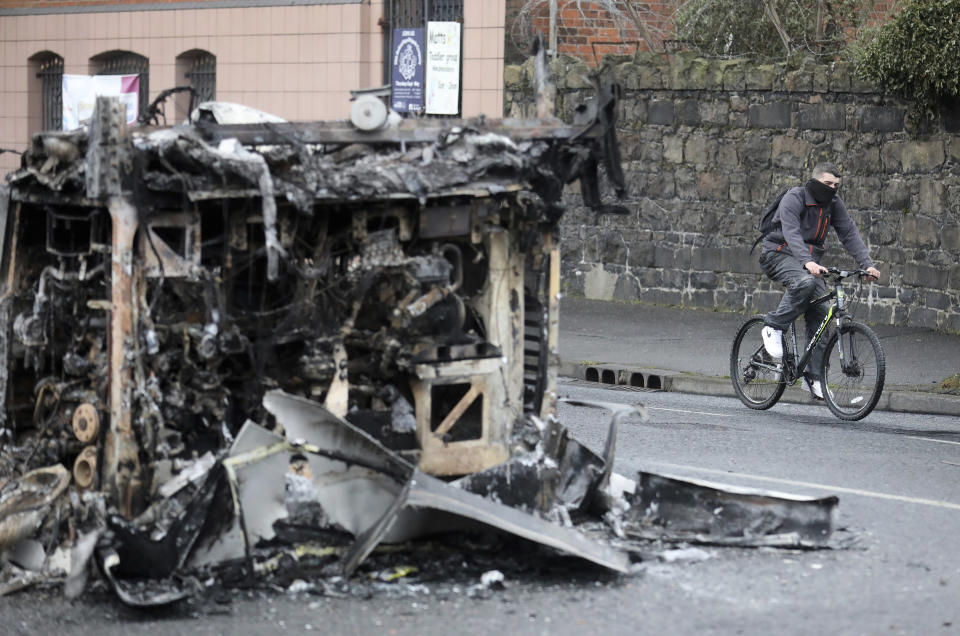 A cyclist passes the remains of a burnt out bus on the Shankill road in West Belfast, Northern Ireland, Thursday, April 8, 2021. It follows another night of violence in Loyalist areas that has now spread to interface areas of the peace divide. (AP Photo/Peter Morrison)