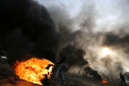 A Palestinian protester moves a burning tire during clashes with Israeli troops at Israel-Gaza border, in the southern Gaza Strip April 5, 2018. REUTERS/Ibraheem Abu Mustafa