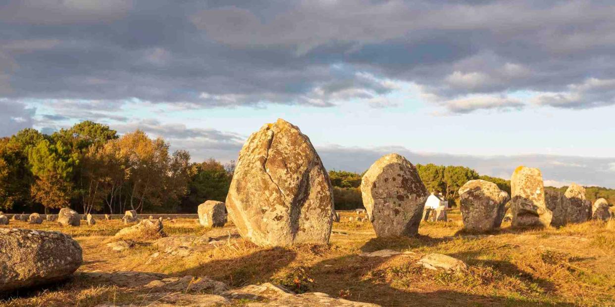 A file image of a line of around five standing stones, in warm sunlight, at Menec, Carnac, Western France.