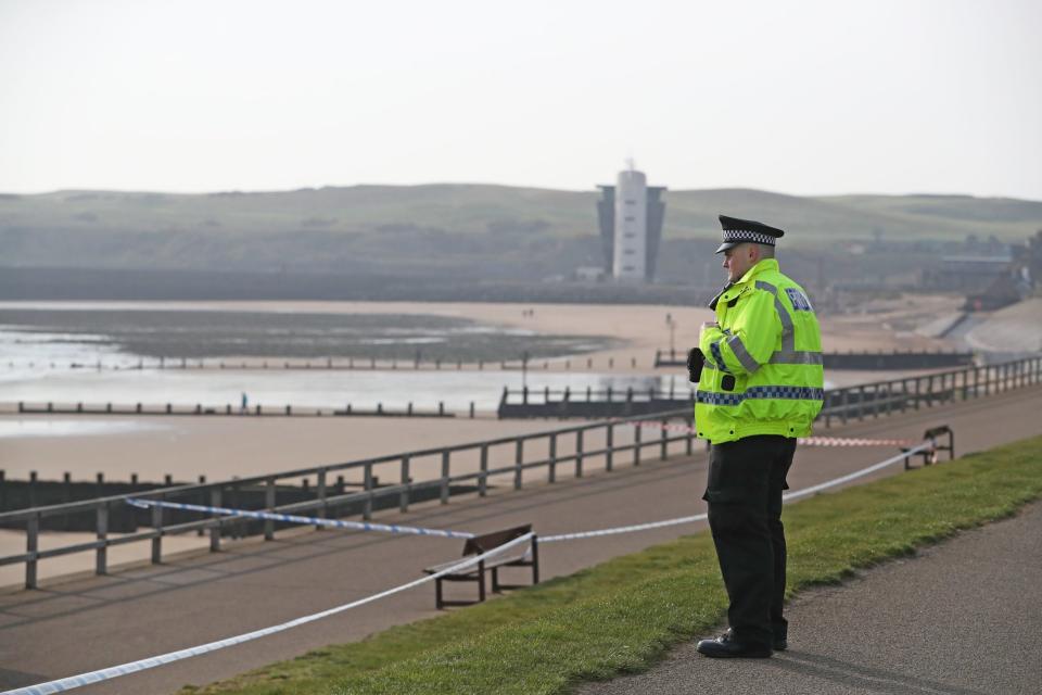 A policeman stands by a cordon at Aberdeen Esplanade where two people were pulled from the sea on Friday (PA)