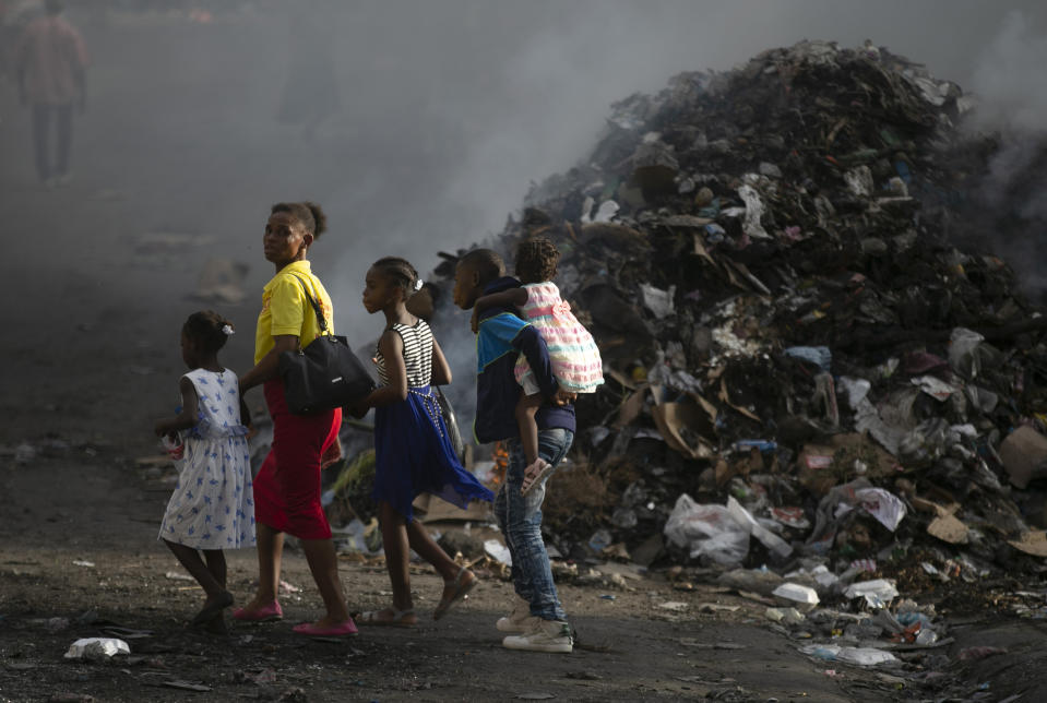 A woman with her children walks next to a smoldering pile of garbage in Port-au-Prince, Haiti, Wednesday, Sept. 28, 2022. (AP Photo/Odelyn Joseph)