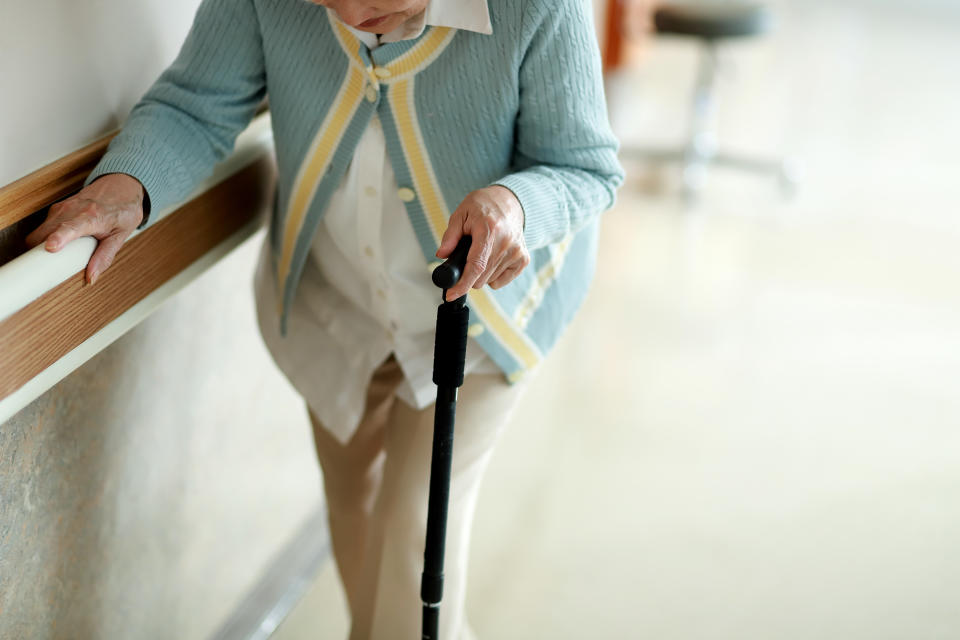 Senior woman walking with walking cane in hospital corridor