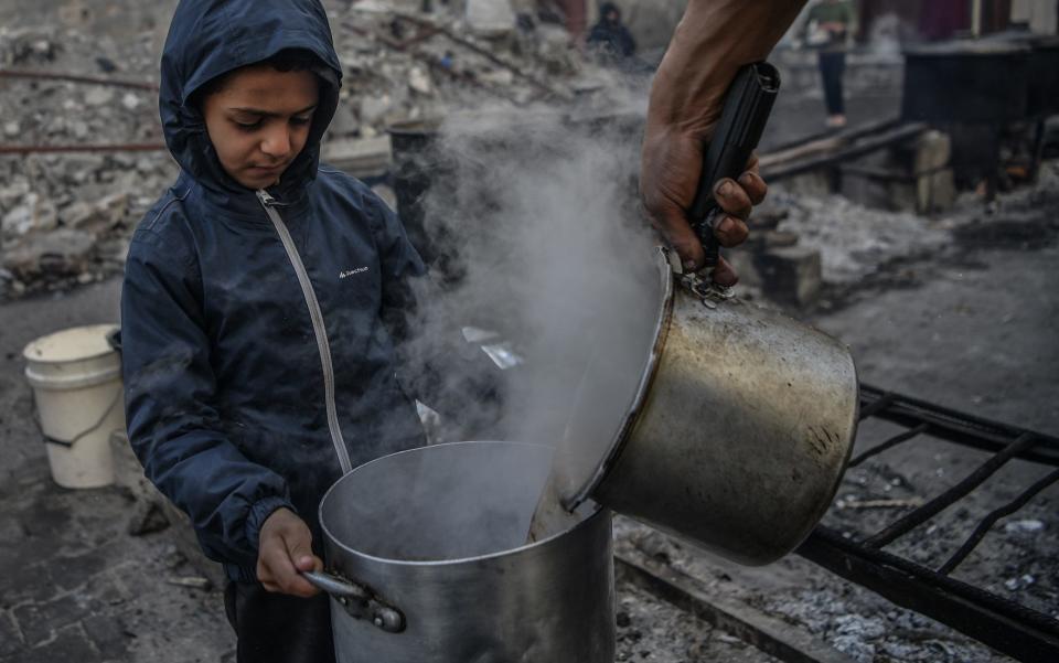 RAFAH, GAZA - DECEMBER 22: A Palestinian child receive food distributed by volunteers for Palestinian families ,displaced to Southern Gaza due to Israeli attacks, between rubbles of destroyed buildings in Rafah, Gaza on December 22, 2023. In the Gaza, where Israeli attacks persist, thousands of Palestinians are grappling with food shortages. The city of Rafah, which has become a refuge for tens of thousands displaced due to the Israeli attacks, is facing increasing challenges in sourcing food. (Photo by Abed Zagout/Anadolu via Getty Images)