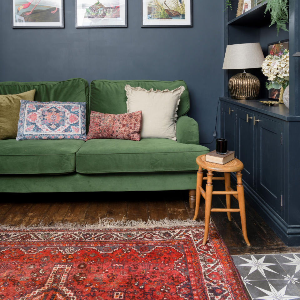 Navy painted wall and cabinet storage area with green sofa, red patterned rug