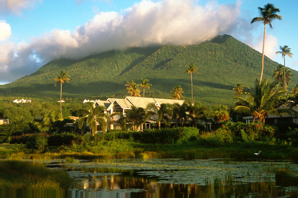 Nevis Peak extinct volcano viewed from lake, with hoouses, palm trees and puffy cloud at peak, Nevis