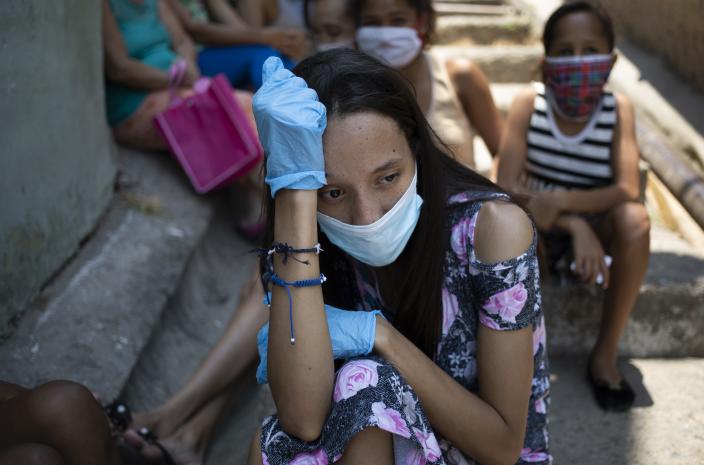 A woman wearing a protective face mask and disposable gloves as a measure to curb the spread of the new coronavirus, waits outside a soup kitchen, in Caracas' Petare slum in Venezuela, Thursday, April 30, 2020. One in every three people faced hunger last year in Venezuela, according to the food agency's 2019 study. Since a quarantine went into effect in mid-March, the first in Latin America, that number has increased. (AP Photo/Ariana Cubillos)