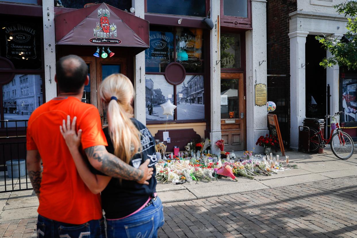 Mourners pause at a makeshift memorial for the slain and injured outside Ned Peppers bar in the Oregon District after a mass shooting that occurred early Sunday morning, Tuesday, Aug. 6, 2019, in Dayton.  Facing pressure to take action after the latest mass shooting in the U.S., Ohio's Republican governor urged the GOP-led state Legislature Tuesday to pass laws requiring background checks for nearly all gun sales and allowing courts to restrict firearms access for people perceived as threats.