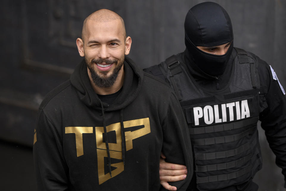 FILE - A police officer escorts Andrew Tate, center, handcuffed, from the Court of Appeal in Bucharest, Romania, Tuesday, March 12, 2024. Romanian court orders trial can start for influencer Andrew Tate on charges of human trafficking and rape. (AP Photo/ Alexandru Dobre, File)