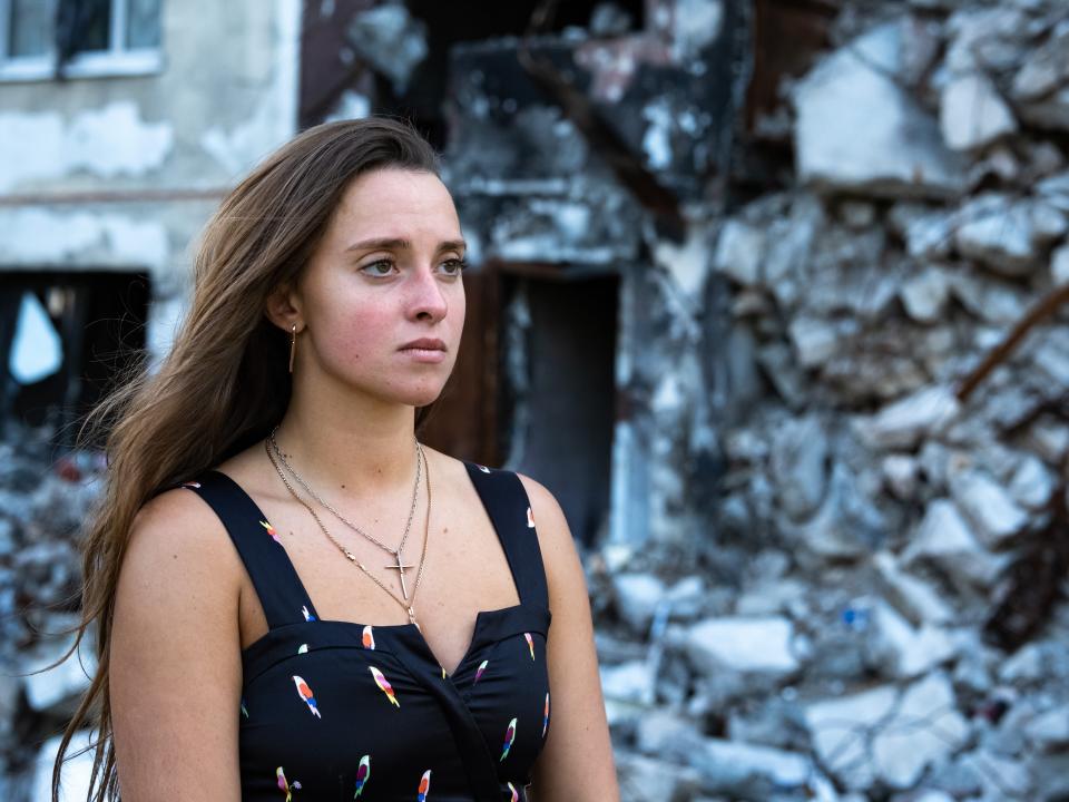 A woman stands in front of ruins in Ukraine.