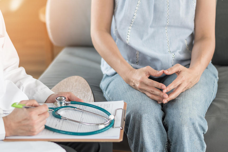 A woman sits beside a doctor writing things down on a clipboard