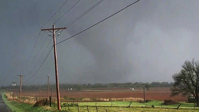 In this image taken from video, a massive funnel-shaped storm cloud makes its way over a road, as seen from a car, in Cole, Okla., Wednesday night, April 19, 2023. Strong storms, including tornadoes, winds and hail, moved through parts of the Central U.S. on Wednesday, causing fatalities and injuries, destroying homes and leaving thousands without power.