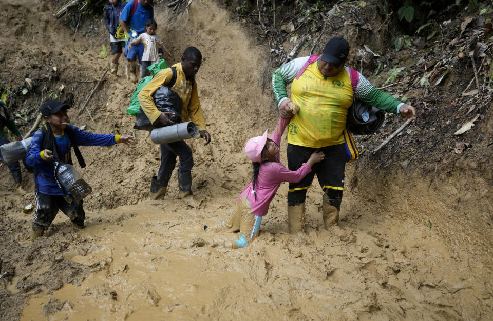 A woman lifts a child from a muddied path as Ecuadorian migrants walk across the Darien Gap from Colombia into Panama hoping to reach the U.S., on Oct. 15, 2022. (AP Photo/Fernando Vergara)