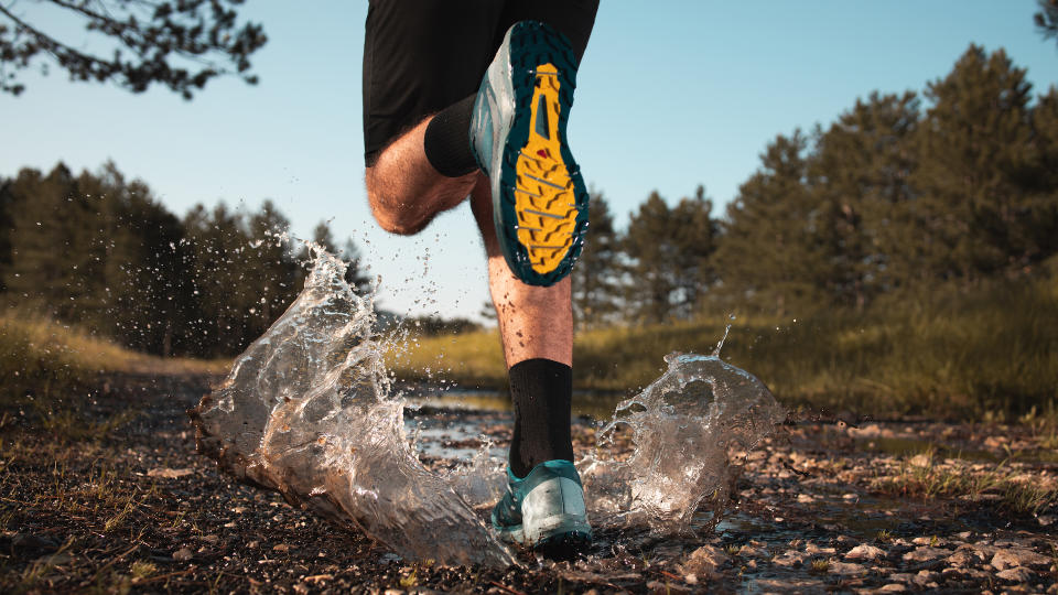 Shot of the legs of a man who is stepping into a puddle while running through the forest.