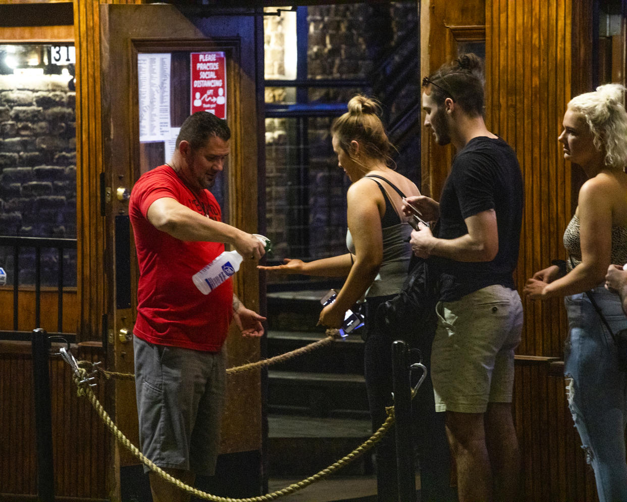 An employee sprays disinfectant on the hands of incoming customers at a bar on Sixth Street at night in downtown Austin, Texas, U.S., on Saturday, May 23, 2020. (Alex Scott/Bloomberg via Getty Images)