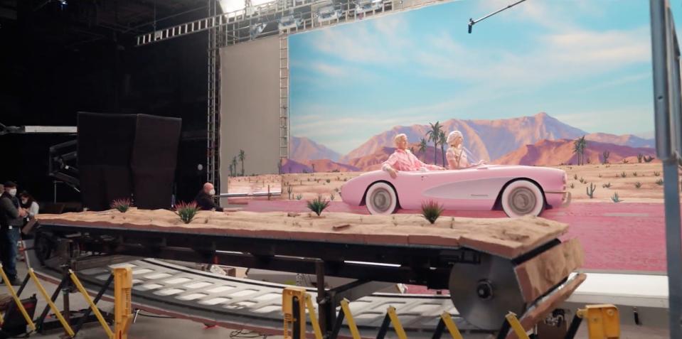 A behind-the-scenes view of the driving scene from the "Barbie" movie, where a large conveyor belt can be seen below the stage.