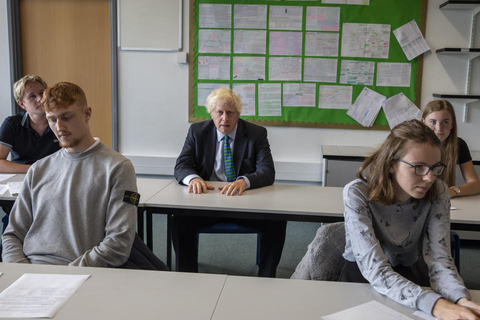 Britain's Prime Minister Boris Johnson sits in a Year 11 class, during a visit to Castle Rock school on the pupils' first day back, in Coalville, East Midlands, England, Wednesday, Aug. 26, 2020. Following mounting pressure to change tack, the British government decided late Tuesday to ditch its advice that high school students in England don’t need to wear face masks while at school. In another in a series of abrupt changes in coronavirus-related policy, the government said children in secondary schools — those above 11 years of age — in areas under local lockdown rules, such as Greater Manchester, will have to don face masks when moving around corridors and communal areas. (Jack Hill/Pool Photo via AP)