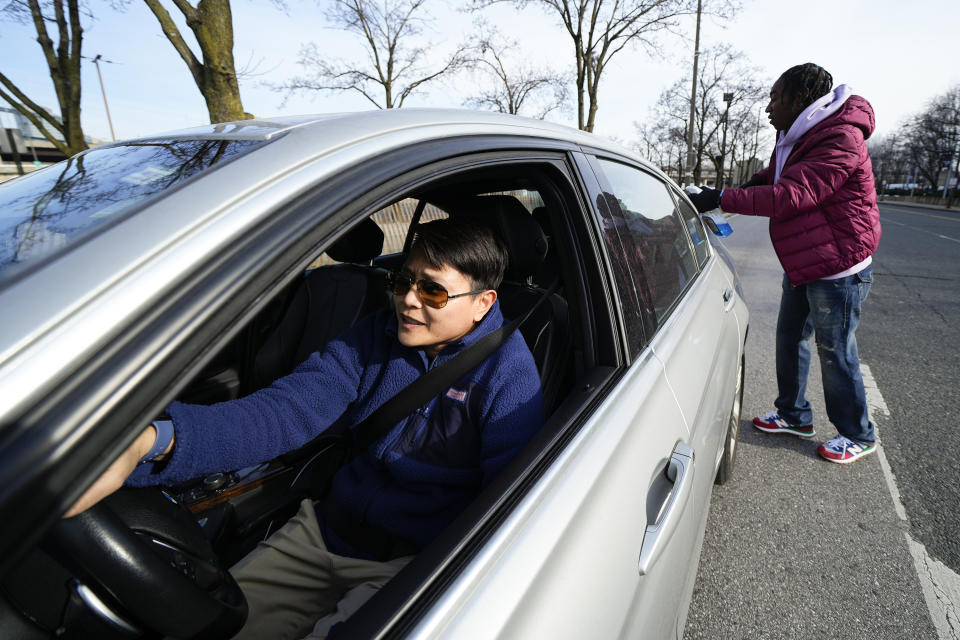 Titi Sangma, left, sits at a traffic signal as Shamonte Jones, right, squeegee cleans the back windshield of her vehicle in exchange for cash, Tuesday, Jan. 10, 2023, in Baltimore. "I see him every day," Sangma said. "He does a good job." Local officials are rolling out their latest plan to steer squeegee workers away from busy downtown intersections and toward formal employment using law enforcement action and outreach efforts. (AP Photo/Julio Cortez)